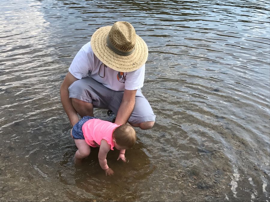 Grandpa in a sun hat helping a baby paddle in the lake
