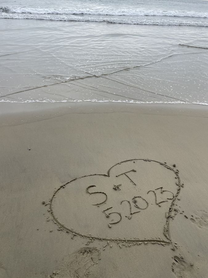 Initials and a date drawn in a heart in the sand by the sea
