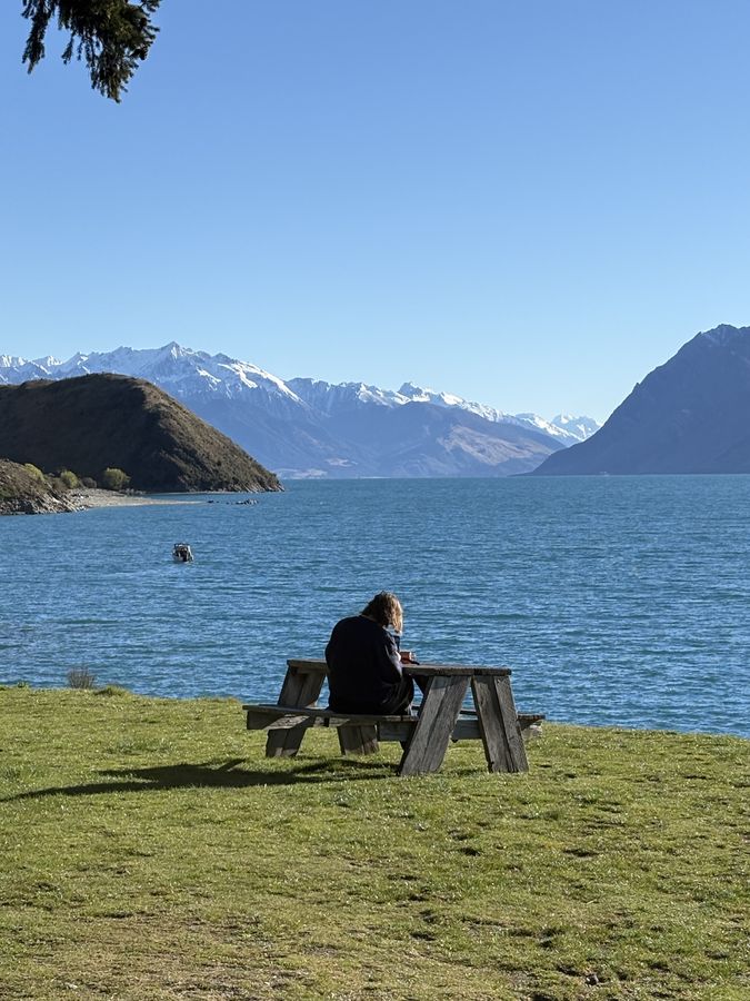 Someone sitting quietly at a picnic table by a mountain lake