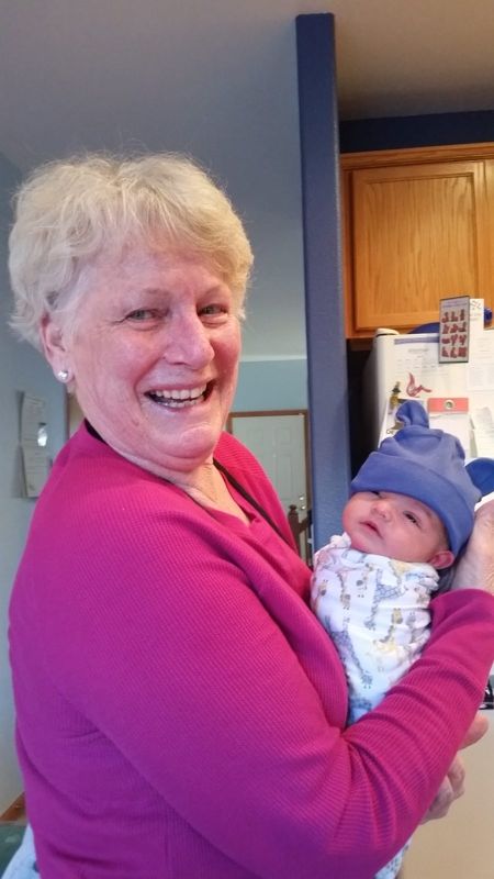 A grandmother laughing as she holds a newborn in a knitted hat