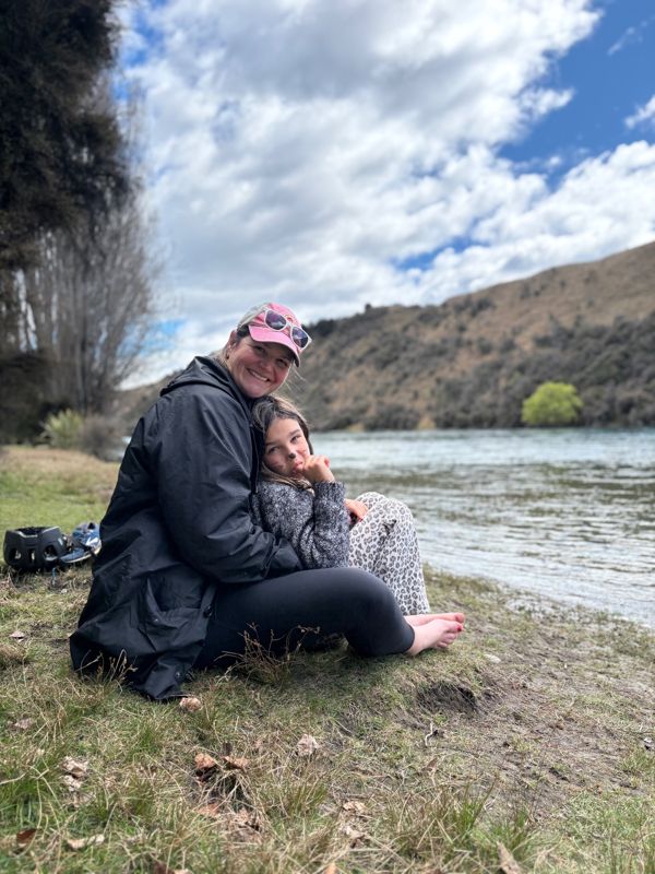 A mum and her daughter cuddled up on a riverbank